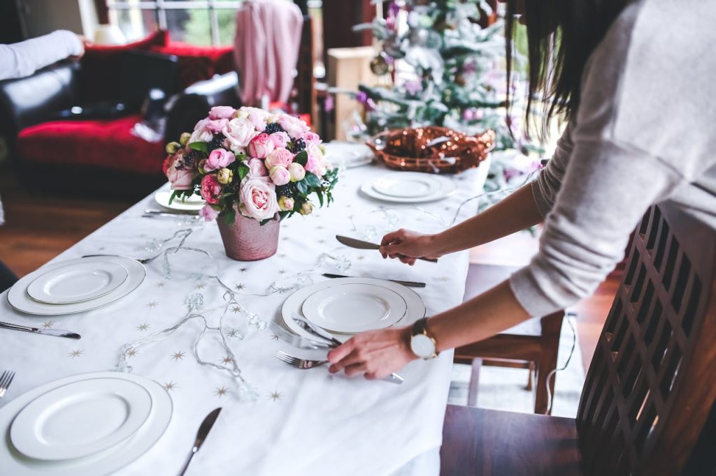 A woman sets a beautifully decorated dining table with flowers for a festive occasion indoors.