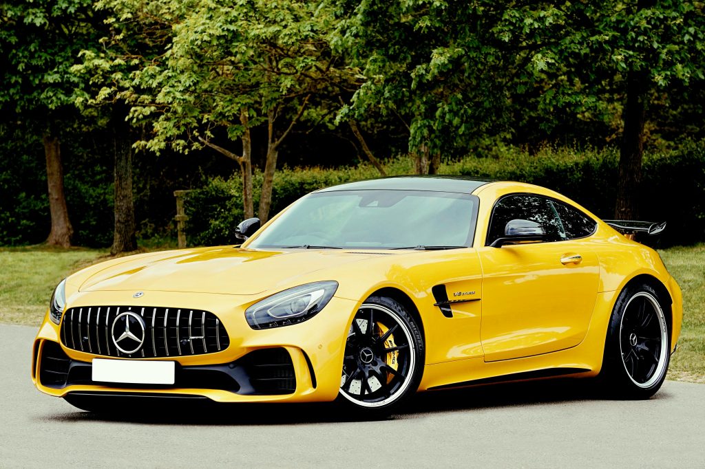 An elegant yellow sports car parked outdoors in a park setting, surrounded by lush greenery.